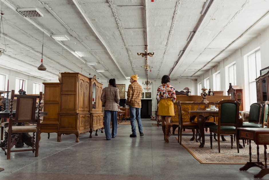 Three people browsing vintage wooden furniture in a spacious store interior with high ceilings.